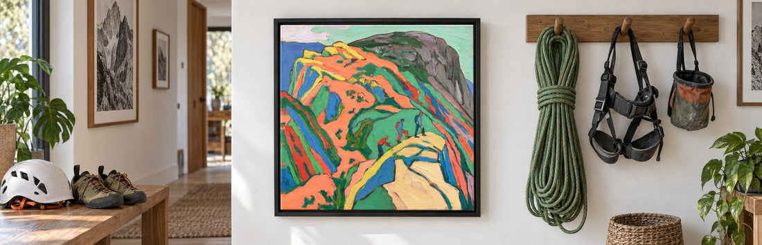 A black-framed canvas of climbers on a bright orange crag in a hallway, beside a climbing rope, harness and chalk bag on wooden pegs