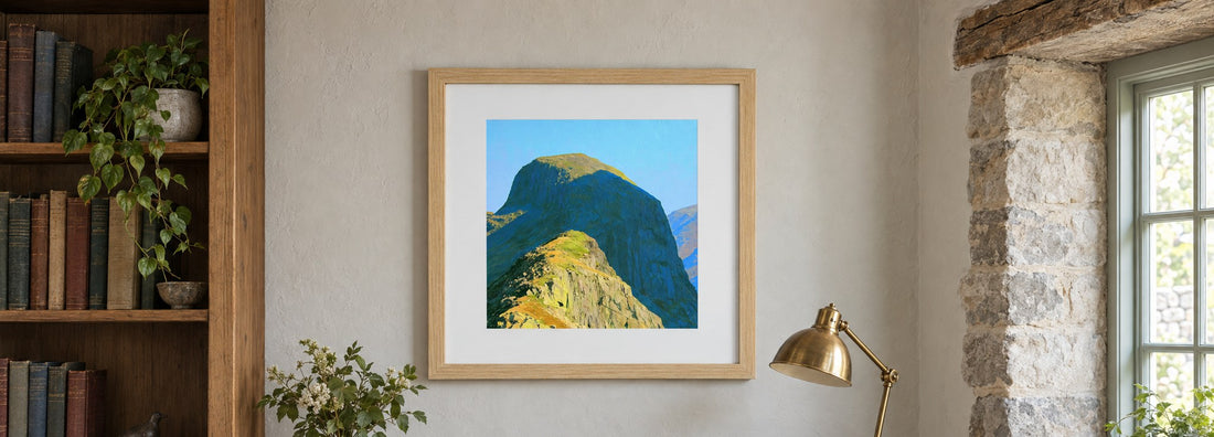 A framed print of the Pike of Stickle with a white mount, hanging above a writing desk in a cottage study